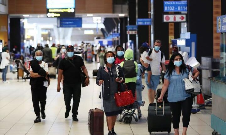 Penumpang yang mengenakan masker pelindung berjalan ke konter check-in di Bandara Internasional Tambo di Johannesburg, Afrika Selatan
