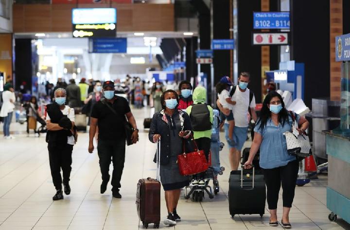 Penumpang yang mengenakan masker pelindung berjalan ke konter check-in di Bandara Internasional Tambo di Johannesburg, Afrika Selatan