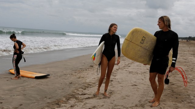 Turis asing membawa papan selancar mereka di pantai Kuta, Bali, Kamis (9/7). Foto: Firdia Lisnawati/AP Photo