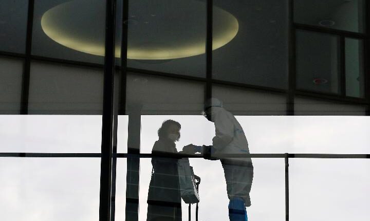 Seorang staf yang mengenakan pakaian pelindung memeriksa suhu seorang penumpang yang naik penerbangan internasional di bandara internasional Narita pada hari pertama penutupan perbatasan untuk mencegah penyebaran virus corona varian Omicron di tengah pandemi penyakit virus corona (COVID-19), di Narita, timur Tokyo, Jepang, 30 November 2021. [REUTERS/Kim Kyung-Hoon]