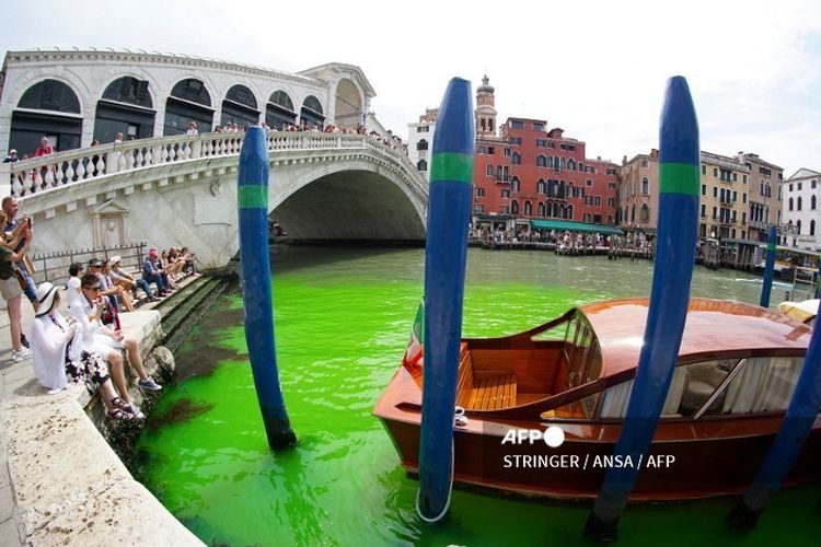 Foto, yang diambil pada Minggu (28/5/2023) oleh kantor berita Italia Ansa, menunjukan perairan berwarna hijau menyala di bawah Jembatan Rialto di Grand Canal di Venesia, Italia. Pertemuan darurat pun digelar pada Minggu (28/5/2023) guna membahas fenomena ini, khususnya terkait asal cairan tersebut.(Dok. Stringer/Ansa/AFP)