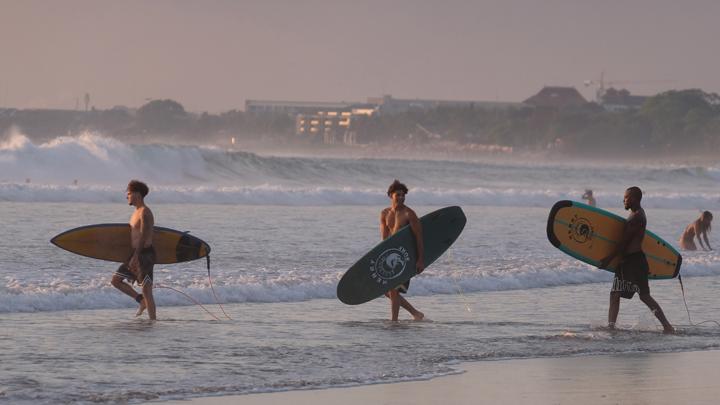 Sejumlah wisatawan membawa papan selancar berjalan menuju ke tengah laut saat berlibur di Pantai Kuta, Badung, Bali, Senin, 25 September 2023. Kepala Dinas Pariwisata Provinsi Bali Tjok Bagus Pemayun mengatakan untuk retribusi sebesar Rp150 ribu kepada turis asing yang masuk Pulau Dewata diterapkan mulai Februari 2024 dan mekanismenya serta tata cara pungutan uang kepada turis asing hingga saat ini masih disusun dalam Peraturan Gubernur (Pergub) Bali. ANTARA FOTO/Nyoman Hendra Wibowo