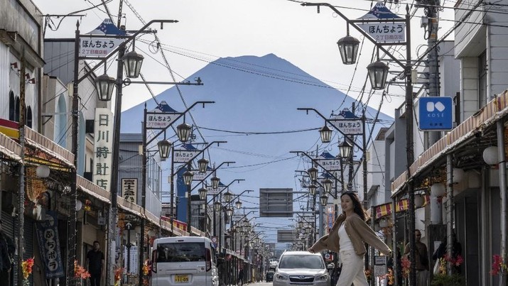 Foto: Warga beraktivitas dengan latar belakang Gunung Fuji, gunung tertinggi di Jepang dengan ketinggian 3.776 meter (12.460 kaki), di Fujikawaguchiko, prefektur Yamanashi pada tanggal 31 Oktober 2024. (AFP/YUICHI YAMAZAKI)