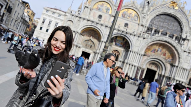 Seorang turis wanita berswafoto bersama seekor burung merpati di St.Mark's Square. Foto: Reuters/Guglielmo Mangiapane